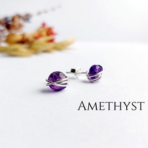 May include: A pair of amethyst gemstone earrings with silver wire wrapped around each stone. The earrings are on a white background with the word "AMETHYST" printed below.