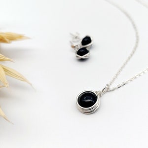 May include: A silver necklace with a black gemstone pendant and matching earrings. The pendant is wrapped in silver wire.