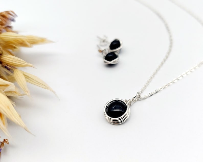 May include: A silver necklace with a black gemstone pendant and matching earrings. The pendant is wrapped in silver wire.