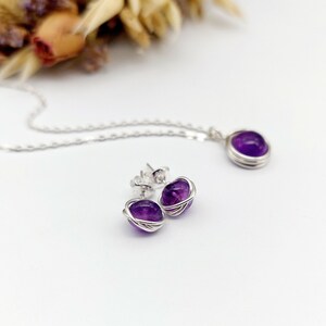 Peut inclure: Un ensemble de bijoux en am&eacute;thyste compos&eacute; d'un collier et de boucles d'oreilles. Les pierres d'am&eacute;thyste sont envelopp&eacute;es de fil d'argent et ont une couleur violet fonc&eacute;.