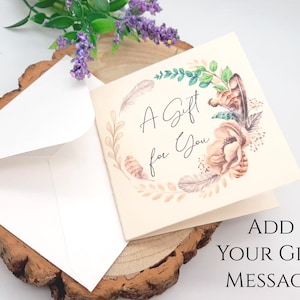 May include: A white card with a floral design and the text "A Gift for You". The card is sitting on a wooden surface with a white envelope.