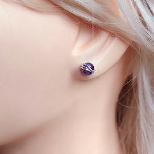 Peut inclure: Une paire de boucles d'oreilles clous en am&eacute;thyste envelopp&eacute;es de fil d'argent. Les pierres d'am&eacute;thyste sont d'une couleur violet fonc&eacute;.