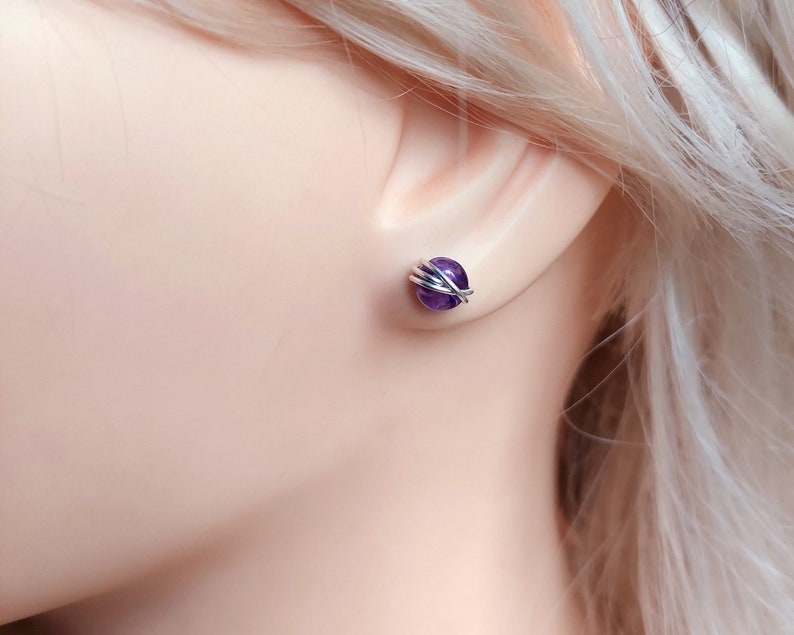 Peut inclure: Une paire de boucles d'oreilles clous en am&eacute;thyste envelopp&eacute;es de fil d'argent. Les pierres d'am&eacute;thyste sont d'une couleur violet fonc&eacute;.