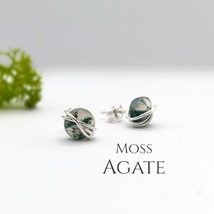 Peut inclure: Une paire de boucles d'oreilles en fil d'argent avec des pierres d'agate mousse. Les boucles d'oreilles sont sur un fond blanc avec le texte "Moss Agate" en dessous.