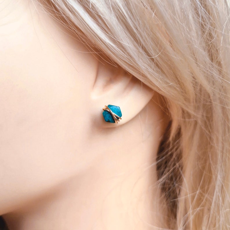 May include: A pair of gold wire wrapped turquoise earrings. The turquoise is a deep blue-green color and the wire is a shiny gold.