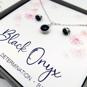 May include: A black onyx necklace and earrings set in a silver wire wrapped design. The jewelry is displayed in a box with the words "Black Onyx" and "Strength. Determination. Balance." printed on the inside.
