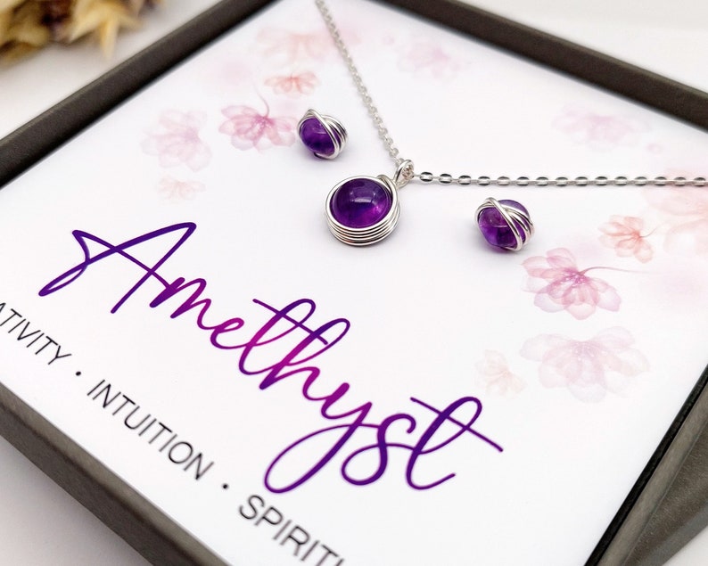 Peut inclure: Ensemble collier et boucles d'oreilles en am&eacute;thyste dans un coffret cadeau. Les bijoux pr&eacute;sentent des pierres d'am&eacute;thyste violettes envelopp&eacute;es de fil d'argent. La bo&icirc;te est orn&eacute;e d'un motif floral et du texte "Am&eacute;thyste" en &eacute;criture violette. Le texte ci-dessous indique "Cr&eacute;ativit&eacute;. Intuition. Esprit."
