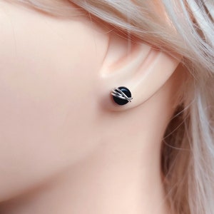 May include: A pair of black onyx stud earrings with silver wire wrapped around the stones.