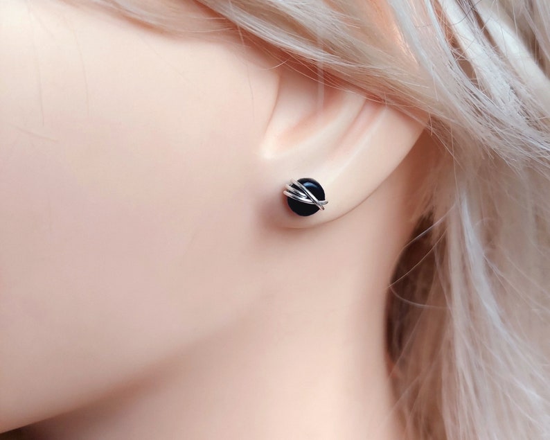 May include: A pair of black onyx stud earrings with silver wire wrapped around the stones.