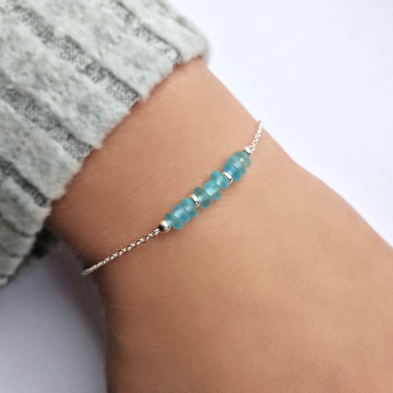 May include: A delicate silver chain bracelet with a row of light blue glass beads.