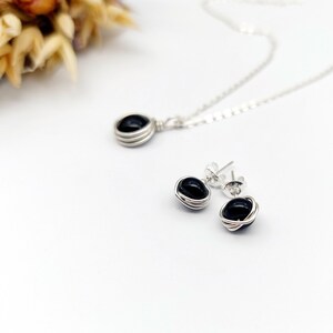 May include: A silver necklace and earrings set with black gemstone pendants wrapped in silver wire.