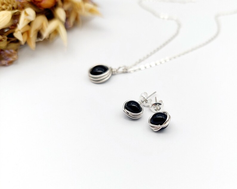 May include: A silver necklace and earrings set with black gemstone pendants wrapped in silver wire.