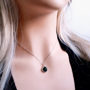 May include: A silver chain necklace with a round pendant featuring a dark green gemstone.