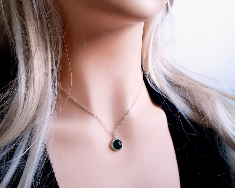 May include: A silver chain necklace with a round pendant featuring a dark green gemstone.
