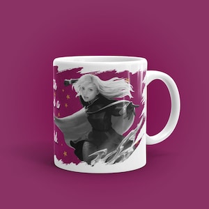 May include: White ceramic mug with a black and white illustration of a woman with long blonde hair, wearing a dark outfit and cape. The mug has the text "With a world". The background is a dark pink.