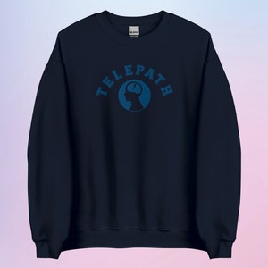 Op de afbeelding: Een donkerblauw sweatshirt met een blauwe afbeelding van een hoofd met het woord "TELEPATH" in een cirkelvormig ontwerp.
