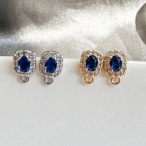 May include: Two pairs of earring findings with a blue oval stone surrounded by clear rhinestones. One pair is silver and the other is gold.