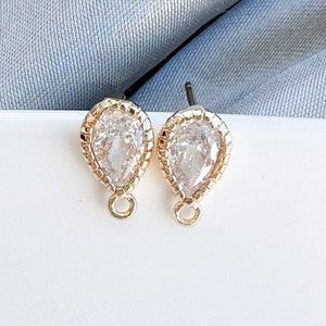 May include: A pair of gold teardrop-shaped earrings with clear crystal stones.