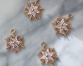 May include: Four gold-colored snowflake charms with clear crystal accents. Each charm has a loop at the top for easy attachment. The snowflake design features six points with crystal embellishments in the center.