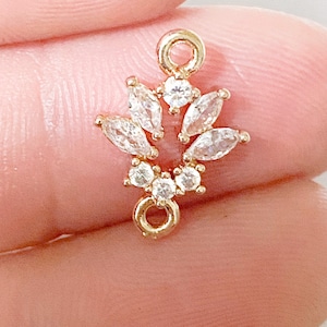 May include: Gold-toned pendant with a cluster of clear cubic zirconia stones in a flower-like design. The pendant has a jump ring at the top and a loop at the bottom.