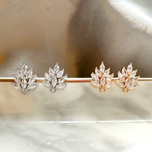 May include: Three pairs of earring findings with a leaf design. The findings are made of silver, gold, and rose gold. Each finding has a loop at the top for attaching earrings.