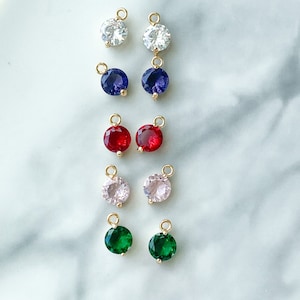 Puede incluir: Surtido de abalorios redondos de piedras preciosas de colores con anillas de salto doradas. Los abalorios son de varios colores, incluyendo blanco, azul, rojo, rosa y verde.