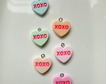 May include: Six heart-shaped charms with the word "XOXO" in pink lettering. The charms are in various pastel colors: light blue, peach, light green, pink, and two shades of cream.