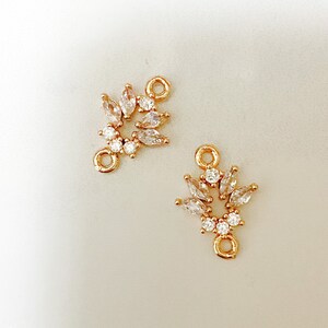 May include: Two gold-toned metal connector charms with clear crystal accents. Each charm features a circular design with a loop on the top.