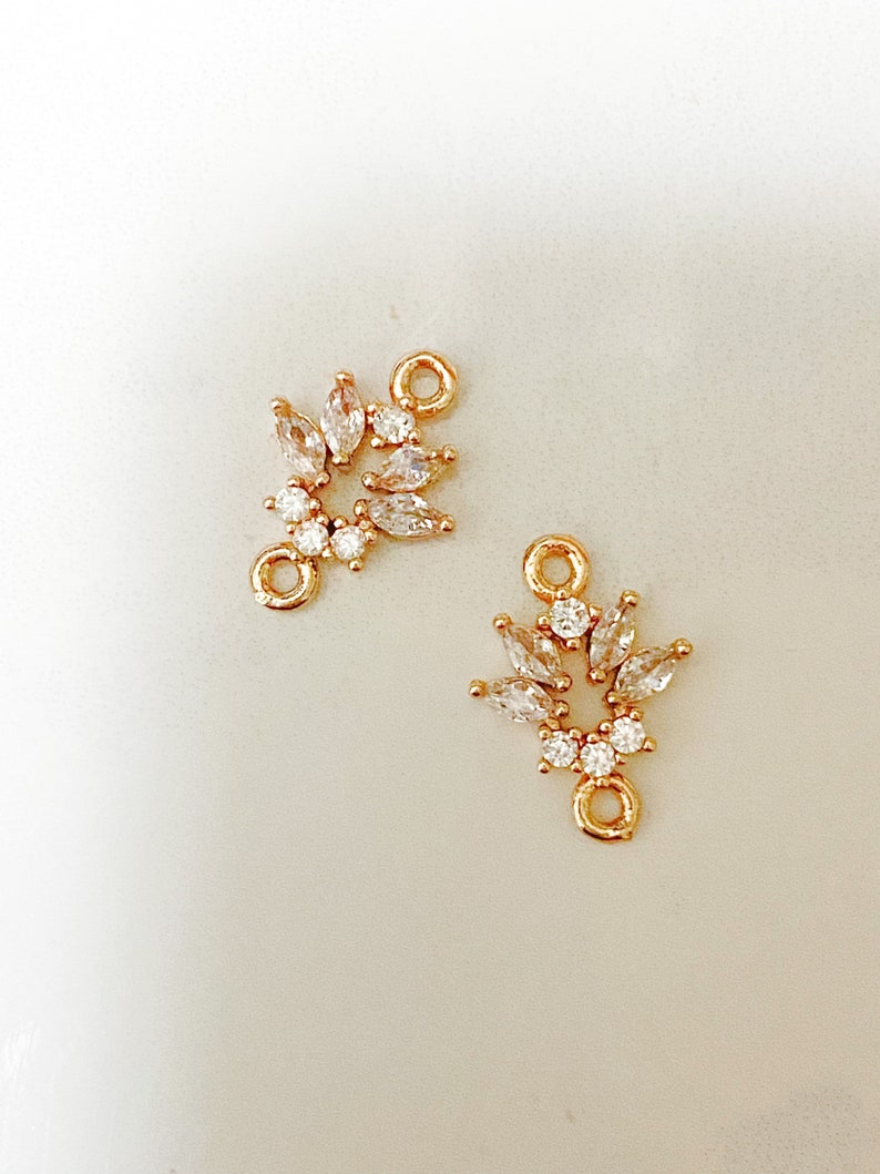 May include: Two gold-toned metal connector charms with clear crystal accents. Each charm features a circular design with a loop on the top.
