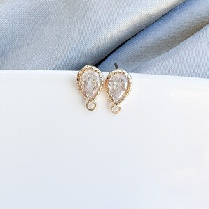 May include: A pair of gold teardrop-shaped earrings with clear crystal stones and a beaded edge.