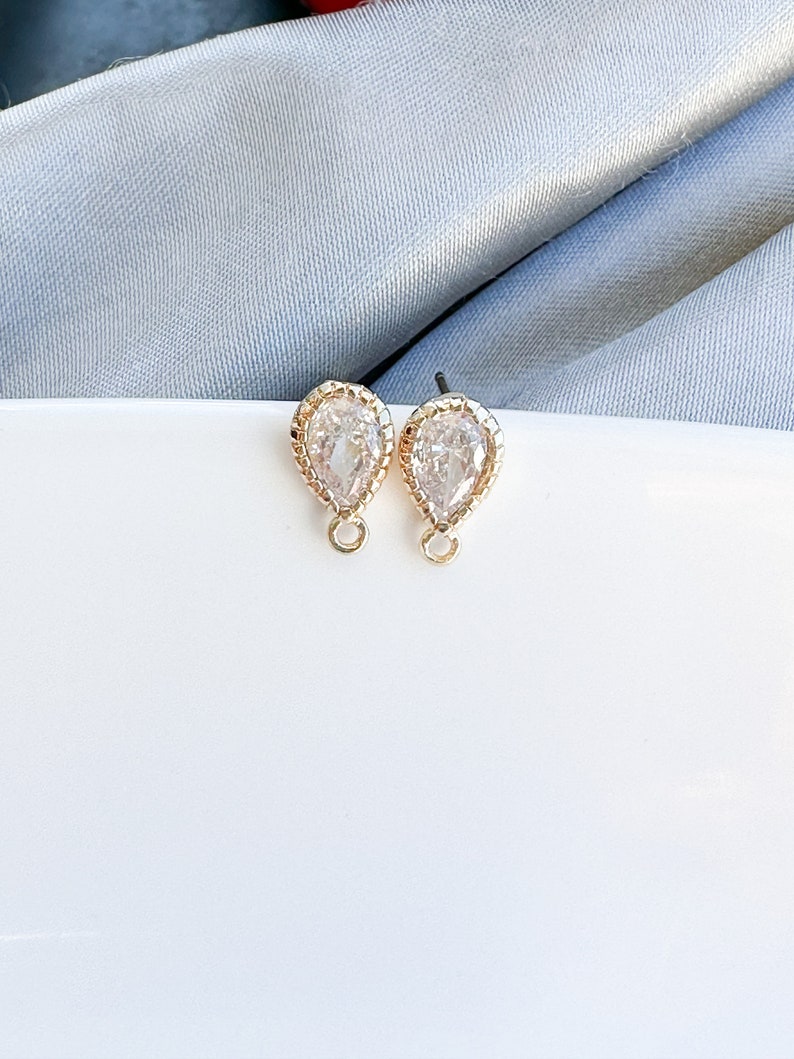 May include: A pair of gold teardrop-shaped earrings with clear crystal stones and a beaded edge.