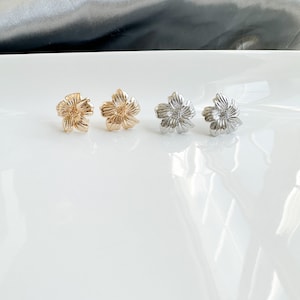 May include: Four flower-shaped earrings, two gold and two silver, displayed on a white surface.