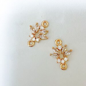 May include: Two gold-tone metal connector charms with clear crystal accents. Each charm features a cluster of marquise-shaped crystals and a round loop.
