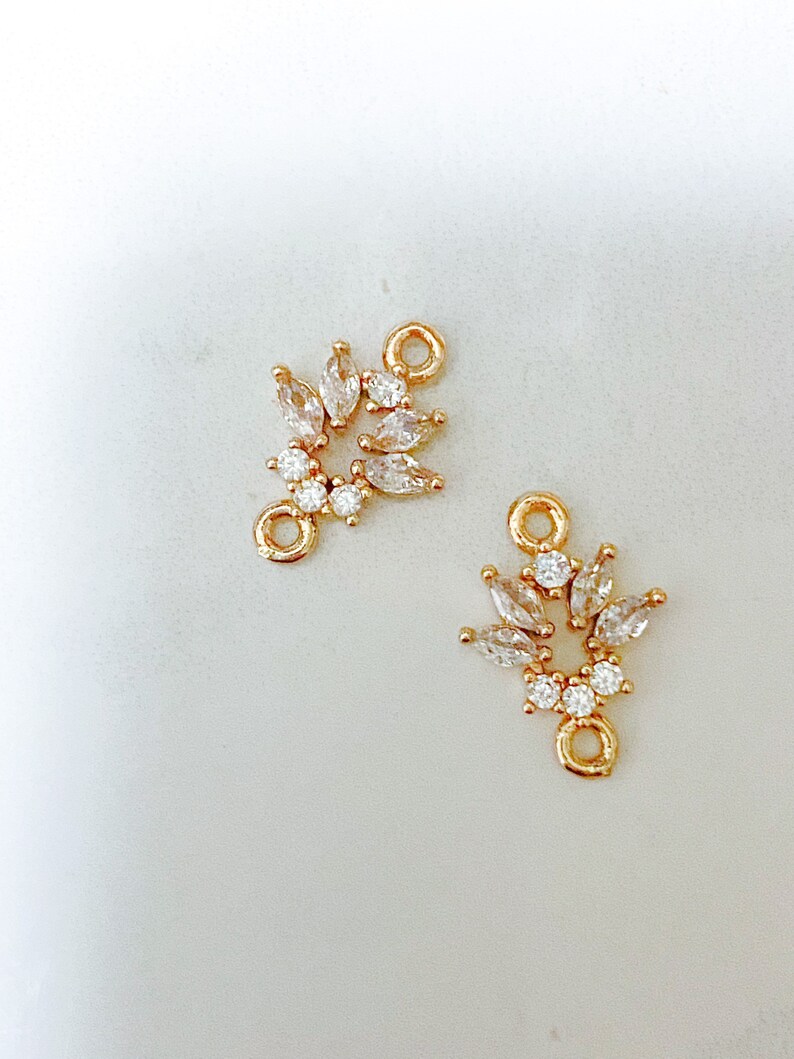 May include: Two gold-tone metal connector charms with clear crystal accents. Each charm features a cluster of marquise-shaped crystals and a round loop.