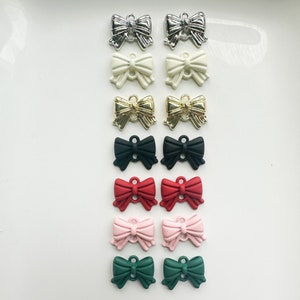 May include: A set of 10 bow-shaped charms in various colors, including silver, white, gold, black, red, pink, and green. The charms are all the same size and shape, and they have a loop at the top for attaching to a necklace, bracelet, or other jewelry.