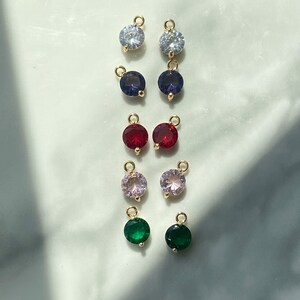 Puede incluir: Surtido de dijes de cristal de colores con anillos de salto dorados. Los dijes son de color transparente, morado, rojo, rosa y verde.