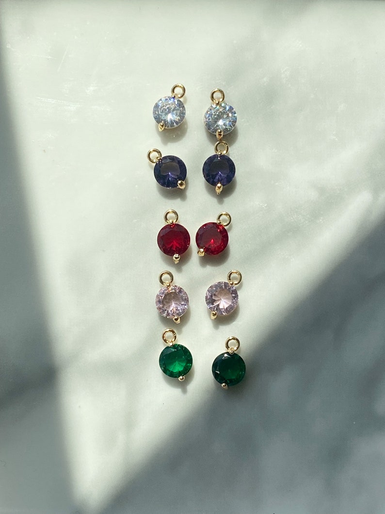 Puede incluir: Surtido de dijes de cristal de colores con anillos de salto dorados. Los dijes son de color transparente, morado, rojo, rosa y verde.
