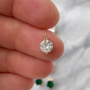 Puede incluir: Un colgante dorado con una piedra redonda de cristal transparente.