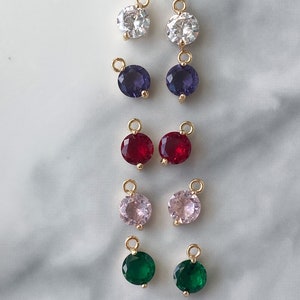 Puede incluir: Diez pares de colgantes de amuleto de tono dorado con piedras preciosas redondas y facetadas. Las piedras preciosas son de varios colores, incluyendo blanco, morado, rojo, rosa y verde.