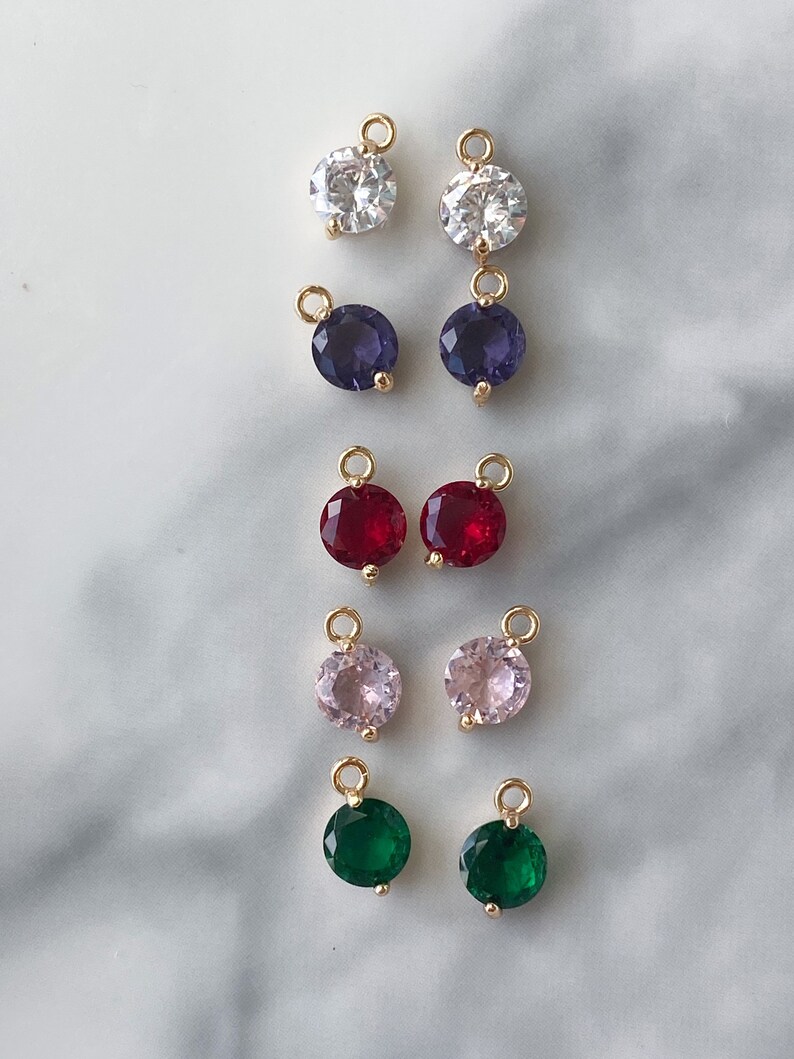 Puede incluir: Diez pares de colgantes de amuleto de tono dorado con piedras preciosas redondas y facetadas. Las piedras preciosas son de varios colores, incluyendo blanco, morado, rojo, rosa y verde.