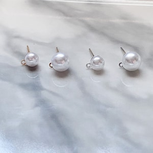 May include: Three pairs of pearl earring findings with gold posts. The pearls are white and round. The findings are different sizes.