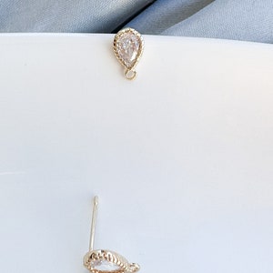 May include: A pair of gold teardrop shaped earrings with clear cubic zirconia stones. The earrings have a beaded edge and a small loop for hanging.