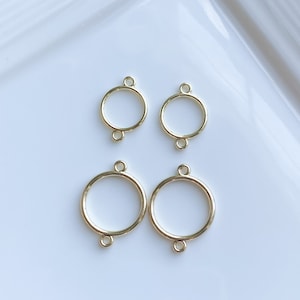 May include: Four gold-colored circular connectors with small loops for jewelry making. The connectors are arranged in a square pattern on a white surface. The connectors are of varying sizes.