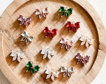 May include: Assortment of colorful rhinestone bow charms in various colors including pink, red, green, and blue. The charms are displayed on a wooden surface.