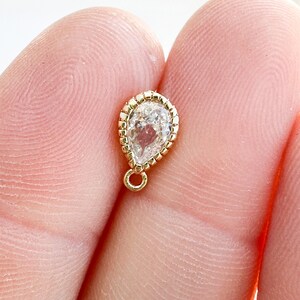 May include: A gold teardrop charm with a clear faceted gemstone and a small loop at the top.