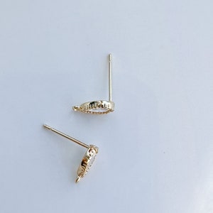 May include: A pair of gold-toned earring posts with a small, round, clear stone set in a decorative bezel. The posts are designed to be inserted into pierced ears.