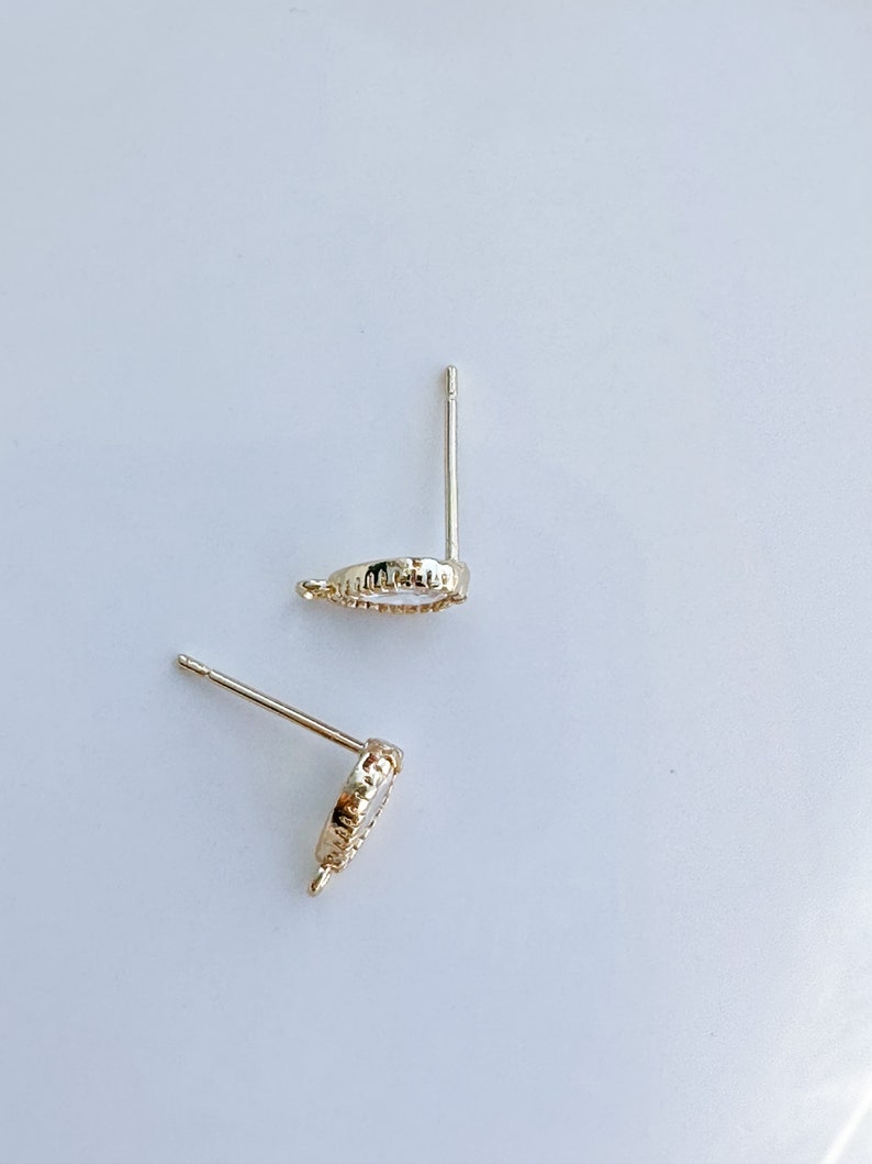 May include: A pair of gold-toned earring posts with a small, round, clear stone set in a decorative bezel. The posts are designed to be inserted into pierced ears.