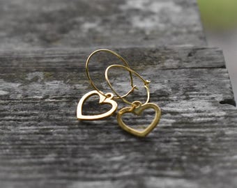 Può includere: Un paio di orecchini a cerchio dorati con un design a forma di cuore.