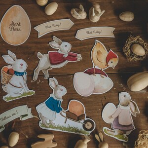 K&ouml;nnte beinhalten: Ein Set an Ostern-Dekorationen mit Hasen, einem K&uuml;ken und Eiern. Die Dekorationen sind auf Karton gedruckt und beinhalten S&auml;tze wie "Hop Hop Hop!" und "Folge mir!"