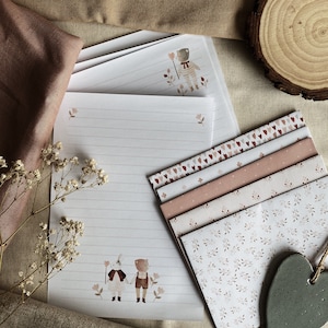 Puede incluir: Un juego de papeler&iacute;a con una ilustraci&oacute;n caprichosa de dos ni&ntilde;os tomados de la mano en un entorno de bosque. El papel est&aacute; rayado y viene con sobres a juego con un delicado patr&oacute;n floral.